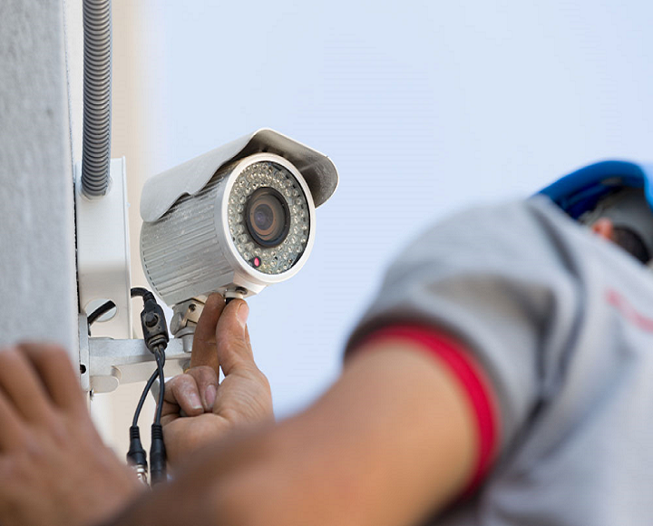 Technician installing CCTV security camera on building wall for surveillance system setup